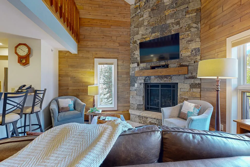 A wood-paneled living room with seating arranged around a stone fireplace and television.