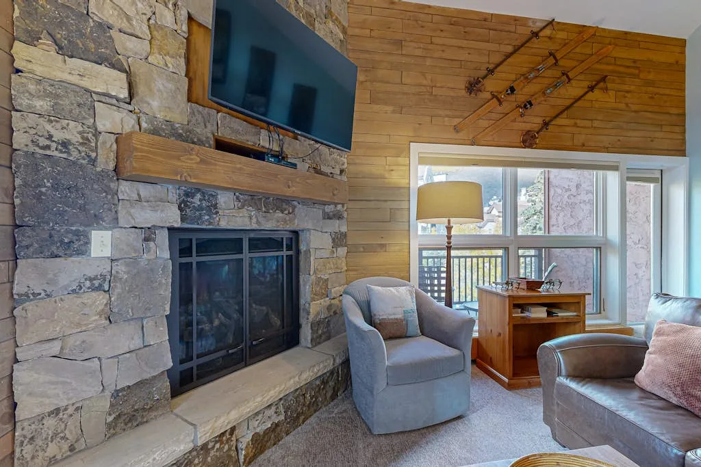 A living room with a stone fireplace, seating, and large windows.