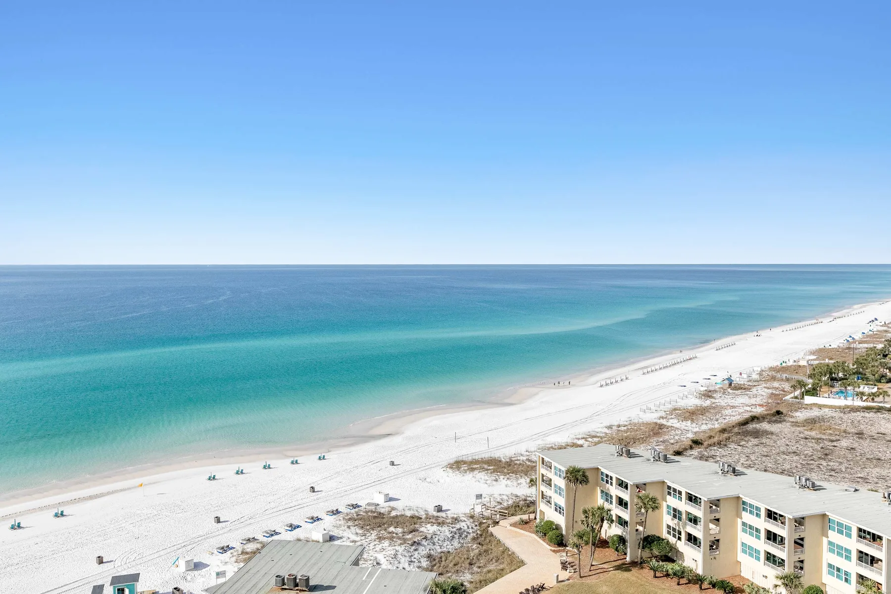 A broad white-sand beach meets clear turquoise water beneath a blue sky.