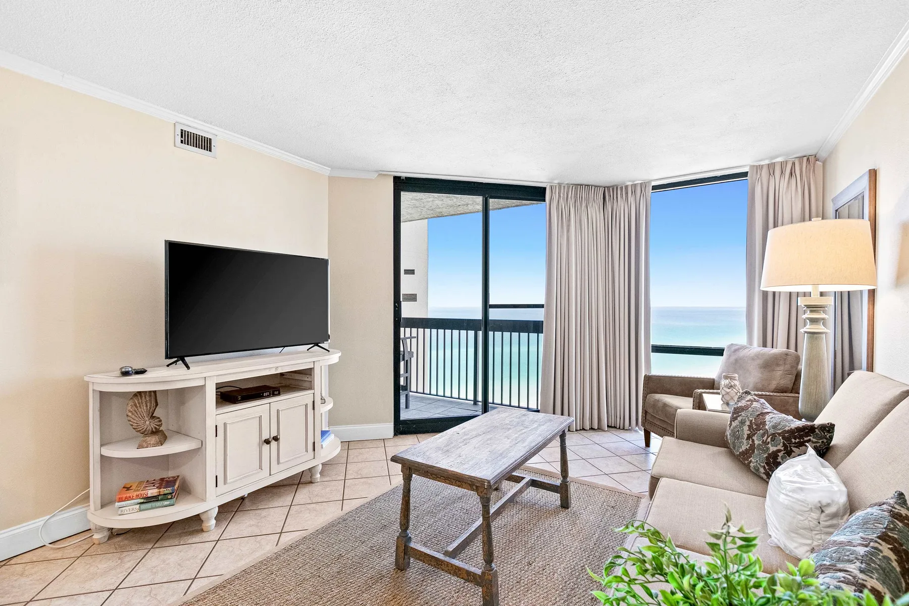 A bright living room with seating, a television, and sliding glass doors overlooking the water.