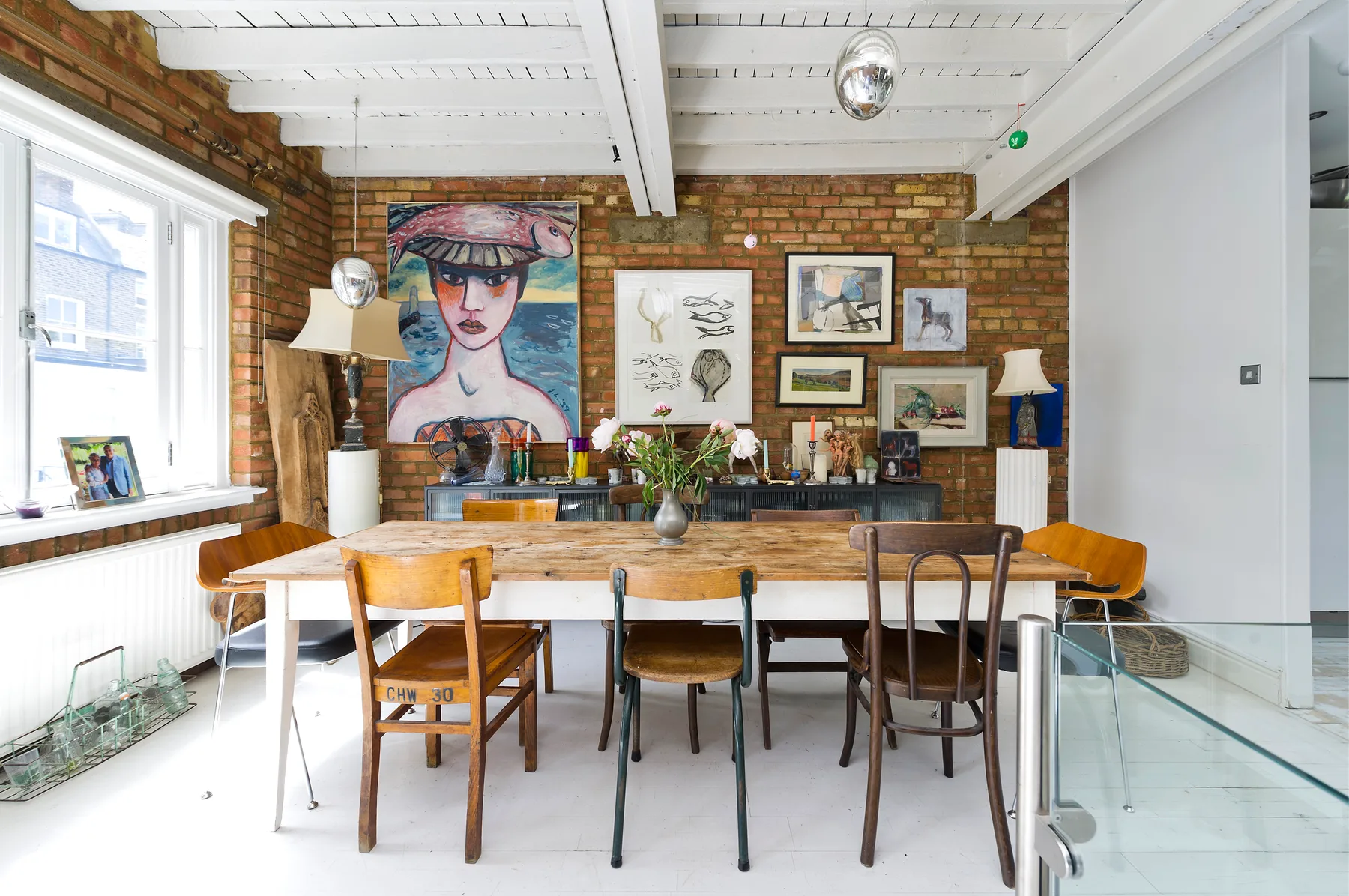 A dining area with a long wooden table, chairs, and colorful artwork on brick walls.