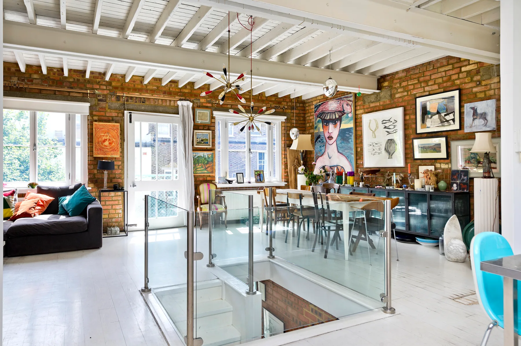 A brick-walled dining and living area has a glass-railed stair opening and large windows.