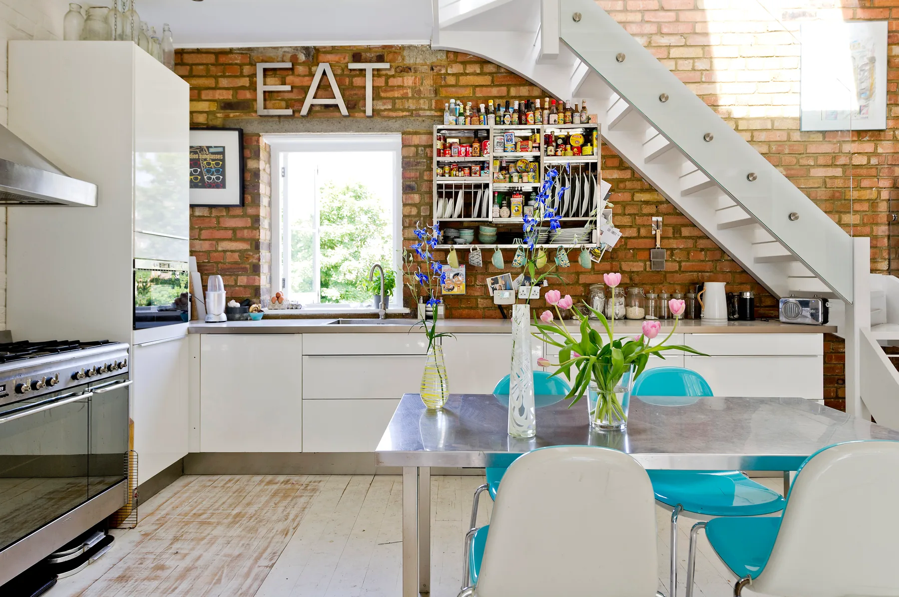 A bright kitchen and dining area with white cabinetry and a table beneath a staircase.