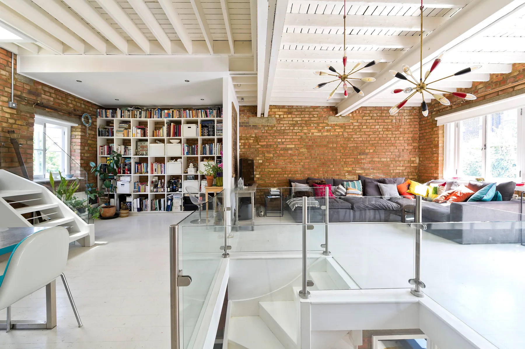 A spacious living room with brick walls, a large bookcase, and seating.
