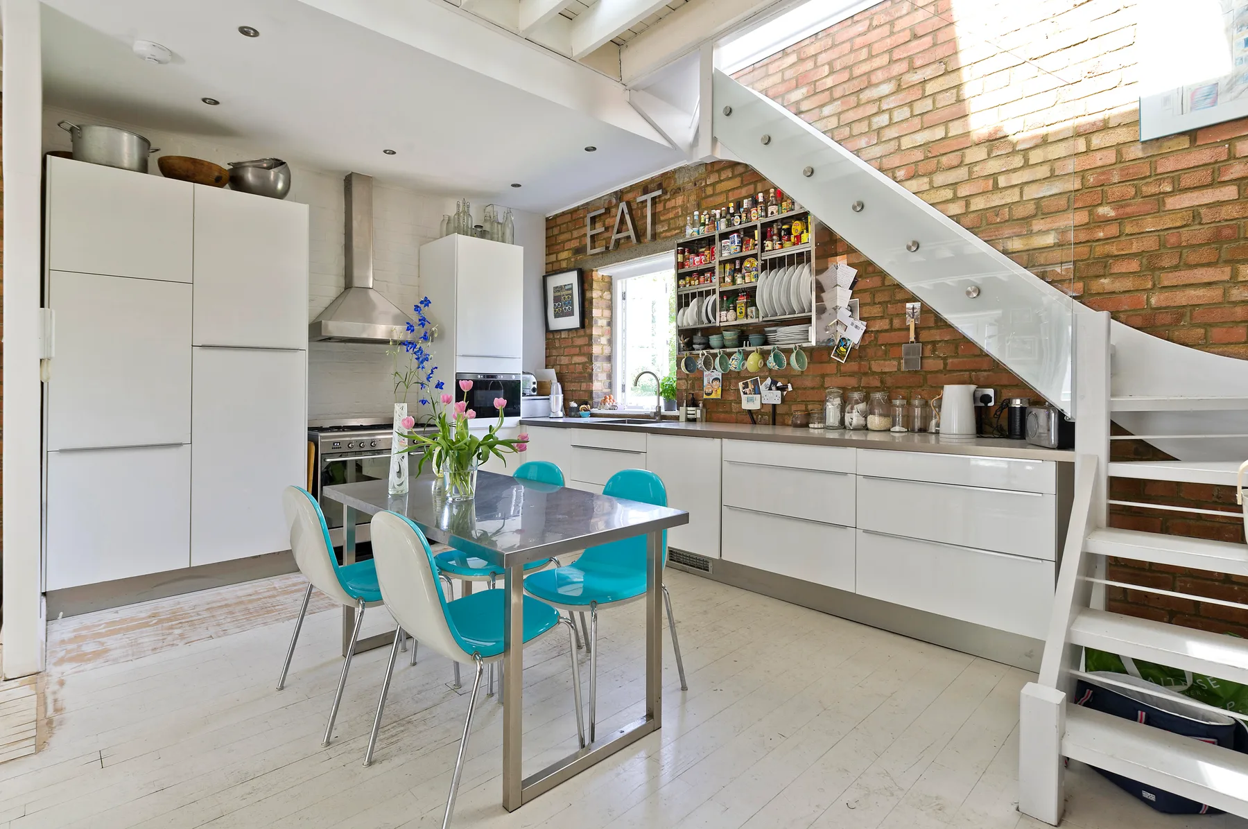 A bright kitchen and dining area with turquoise seating and exposed brick walls.