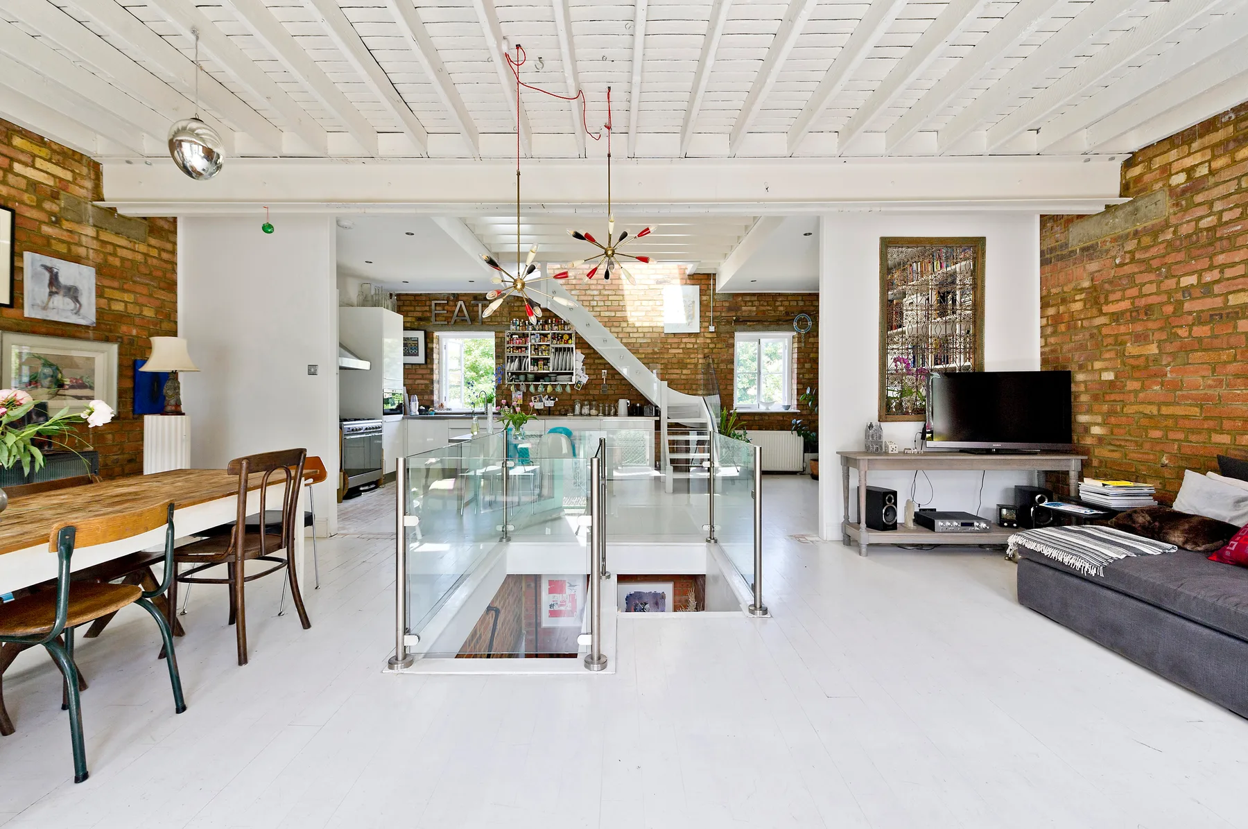 A bright open-plan living area with a dining table, seating, and a glass stair railing.