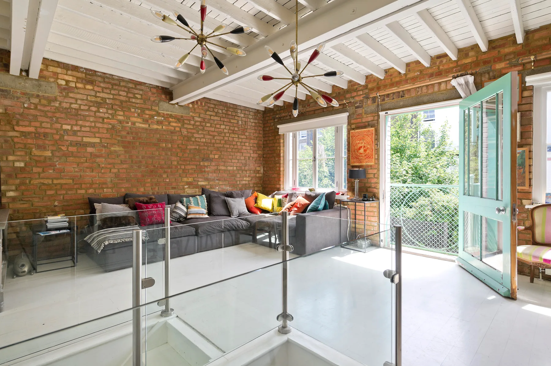 A bright living room with sectional seating, exposed brick walls, and an open glass door.