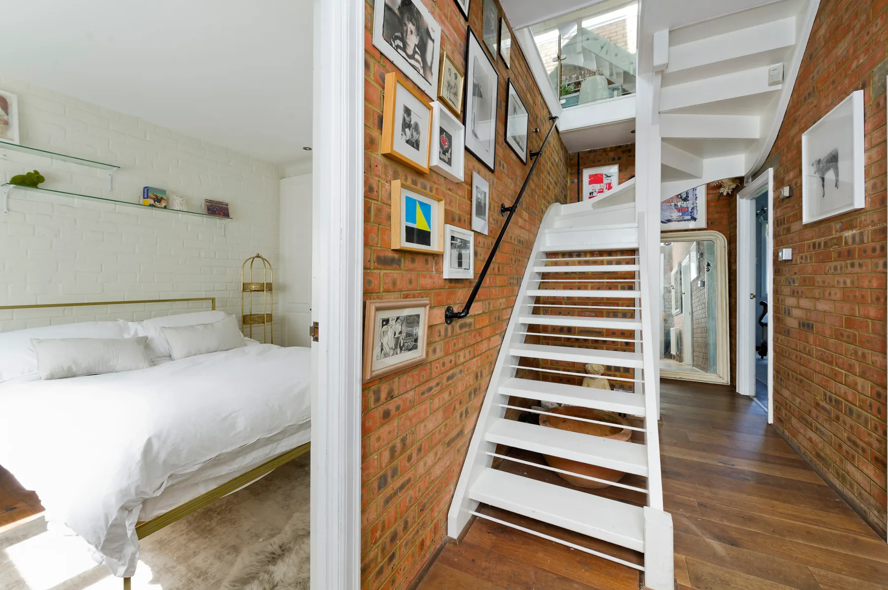 A bedroom with white bedding opens onto a brick hallway and staircase.