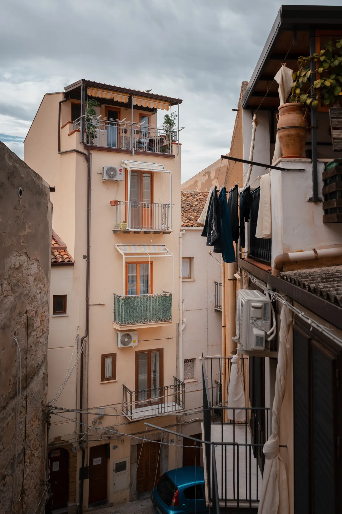 A narrow residential street lined with tall buildings, balconies, and hanging laundry.