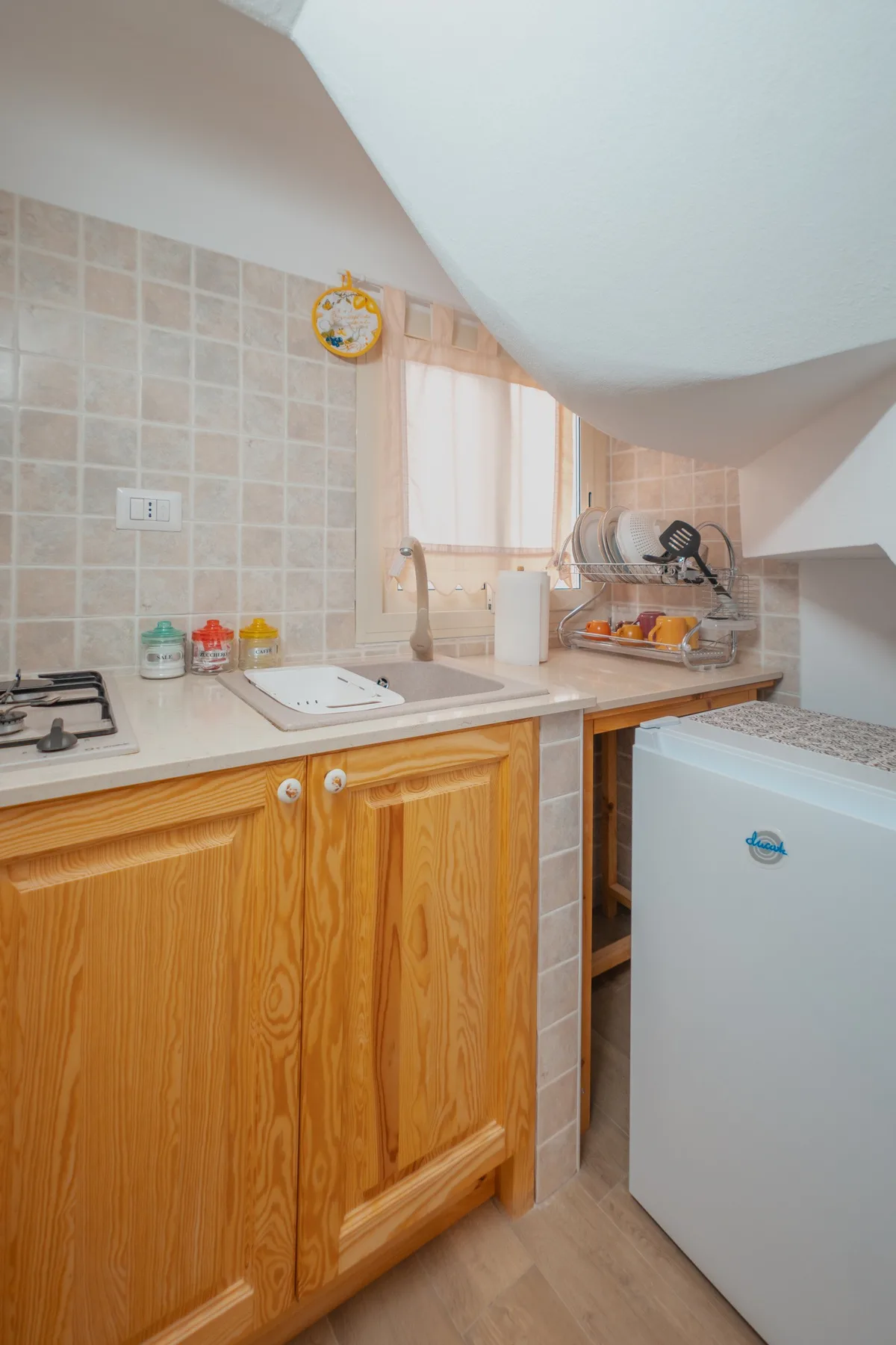 A compact kitchen with wooden cabinets, a sink, and a countertop dish rack.