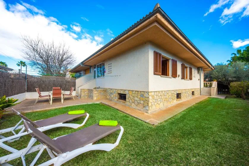 A single-story house with a stone base stands beside a green lawn and patio.