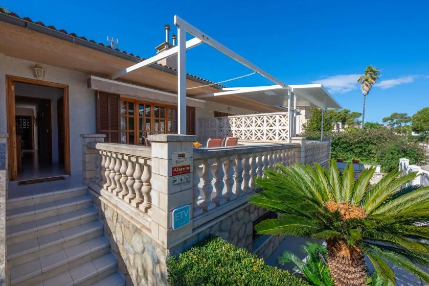 A house terrace with stone railings, outdoor seating, and a palm plant.