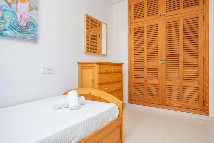 A bedroom with a wooden bed, dresser, and louvered closet doors.