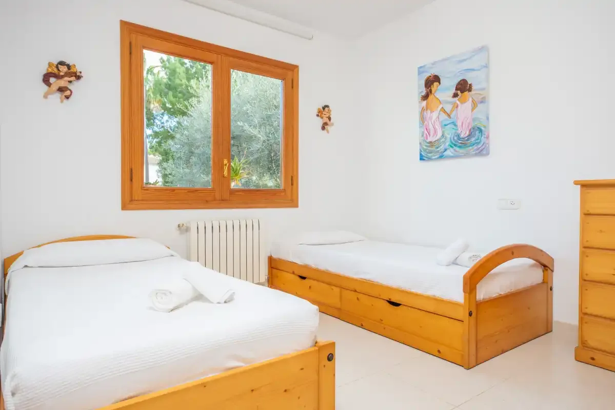 A bright bedroom with two beds and a window overlooking greenery.