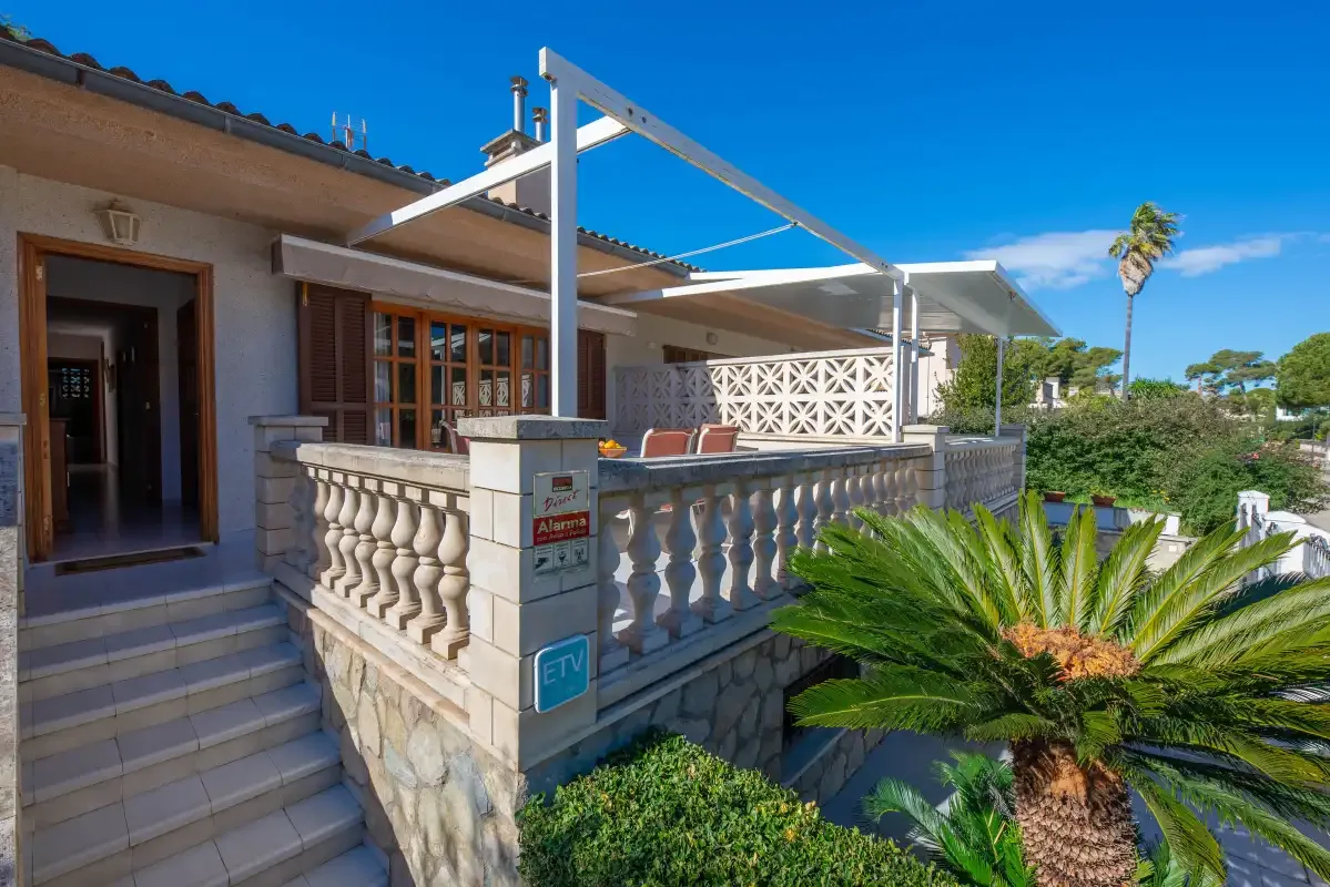 A sunny outdoor patio with stone balustrades, seating, and a white pergola.