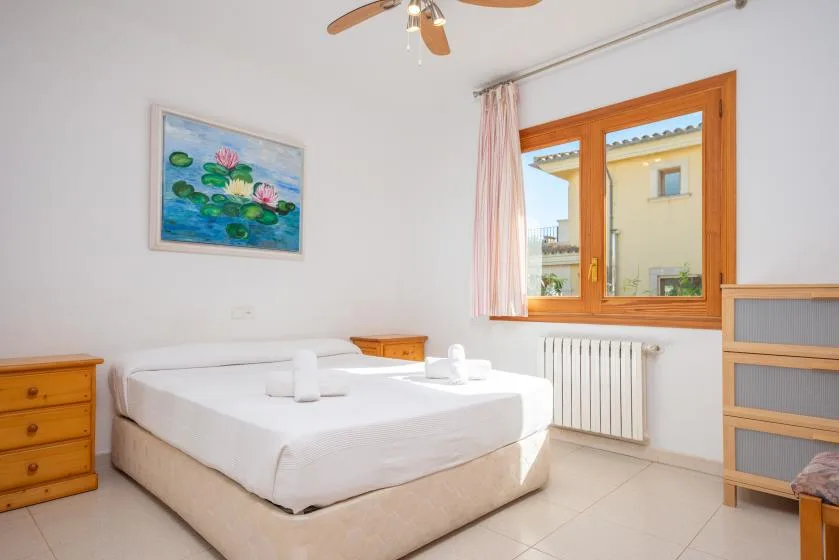 A bright bedroom with a white bed, wooden window, and framed floral painting.