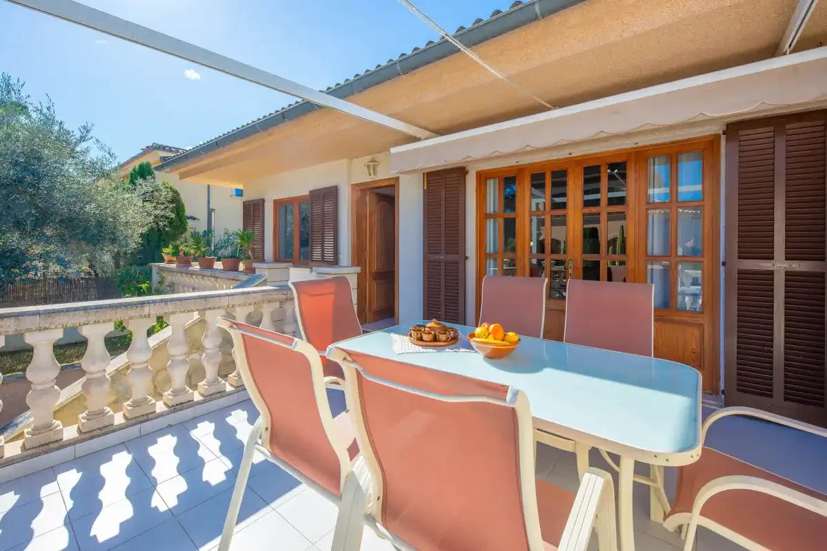 An outdoor dining area with a table and seating beside shuttered doors.