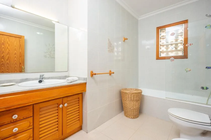 A bright bathroom with a wooden vanity, sink, and glass shower.