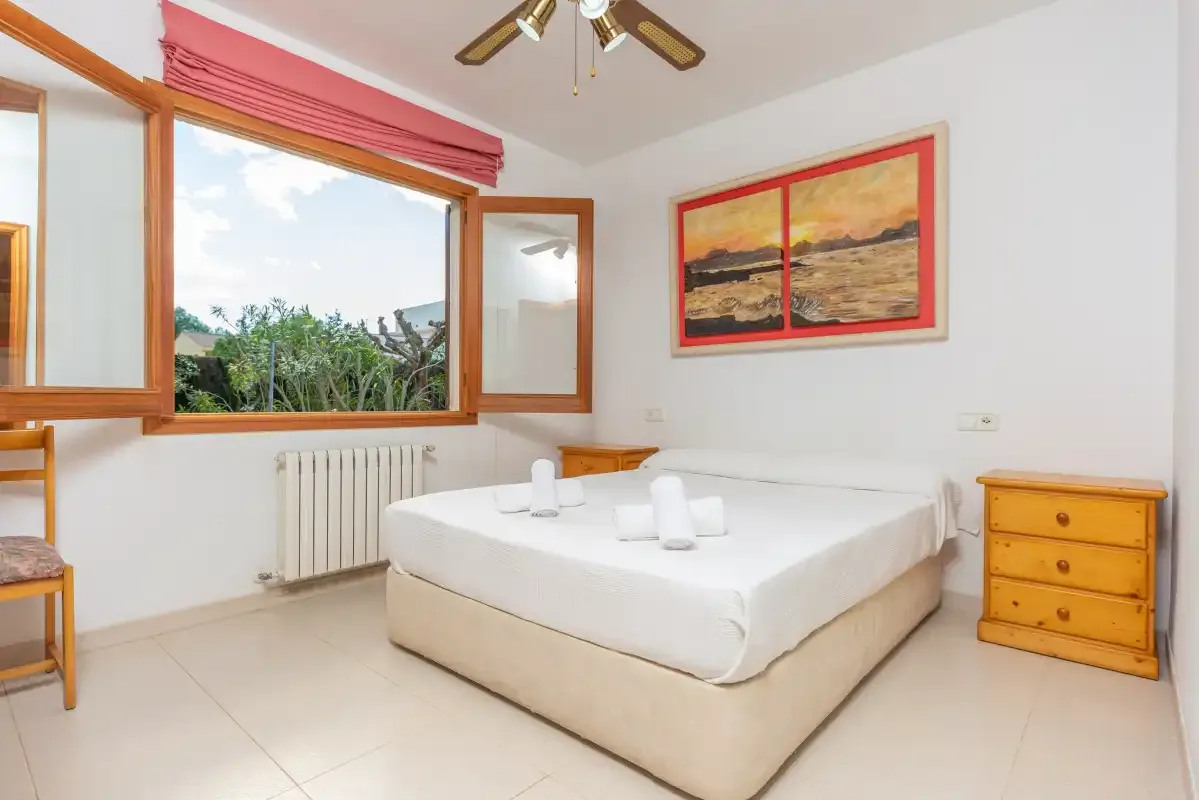 A bedroom with a double bed, an open window, and a wooden dresser.