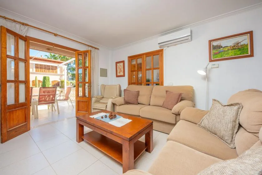 A living room with beige seating and open wooden doors leading to a patio.