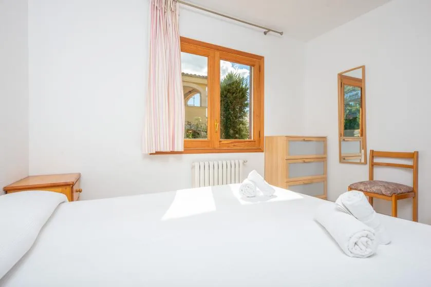 A bright bedroom with a bed, wooden-framed window, and simple furnishings.