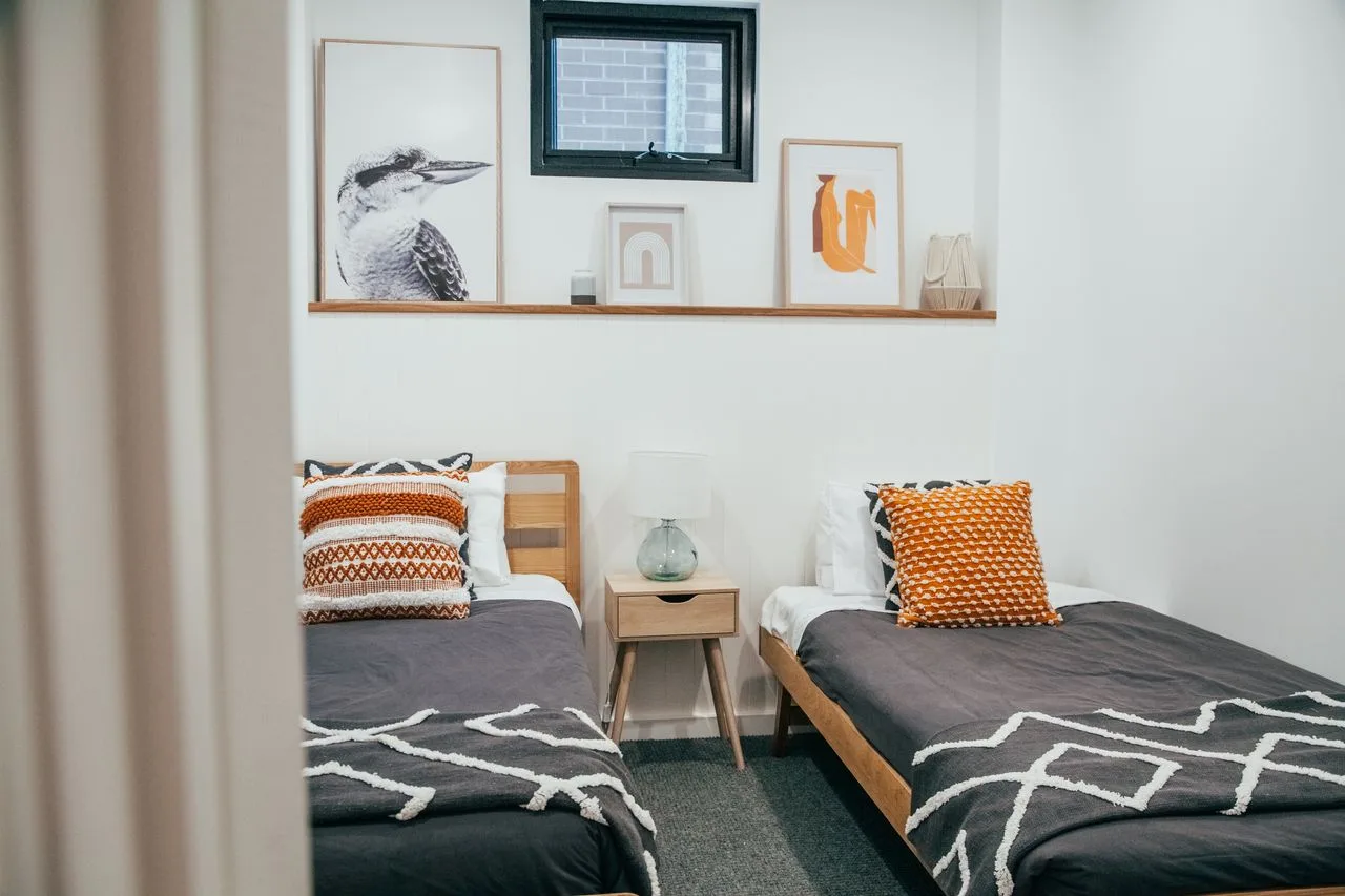 Un dormitorio con dos camas, ropa de cama oscura y cuadros en la pared.
