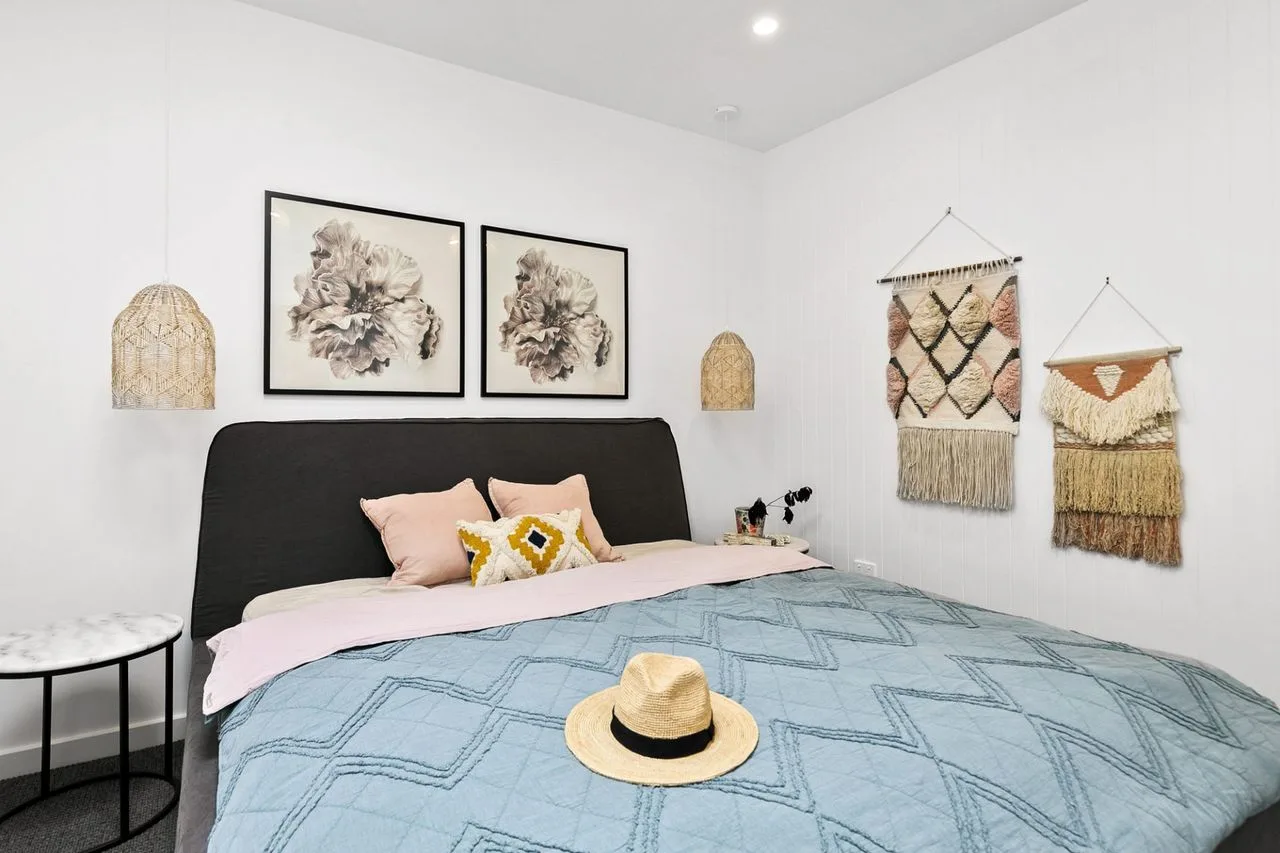 Un dormitorio con una cama, cuadros florales y tapices tejidos.