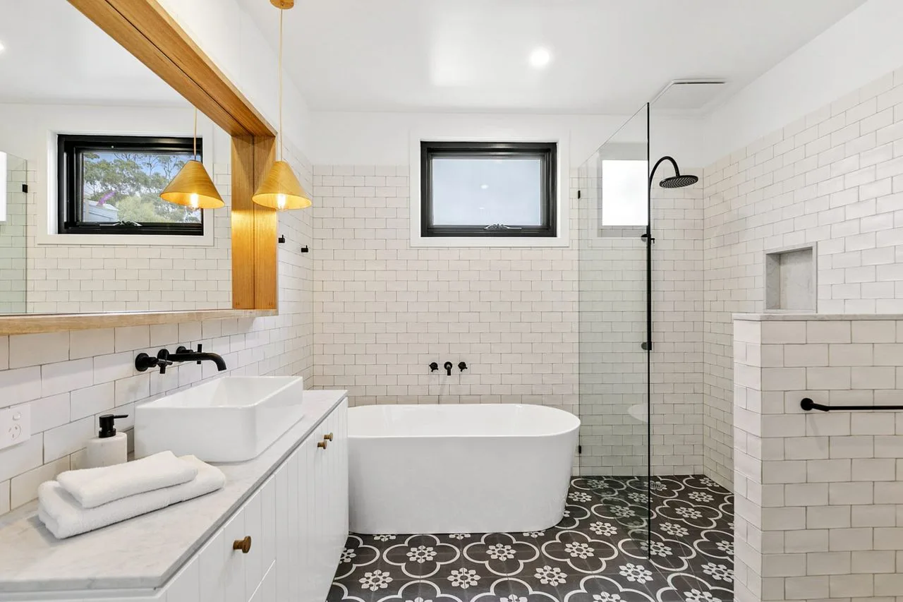 Un baño luminoso con bañera, mampara de ducha de vidrio y paredes de azulejos blancos.