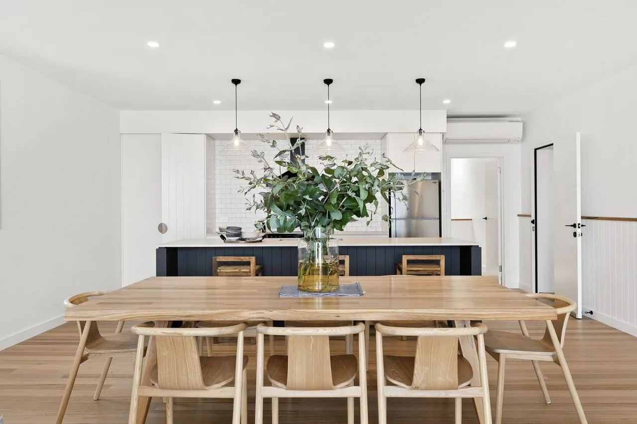 Un comedor luminoso con una mesa larga de madera y un centro de hojas.