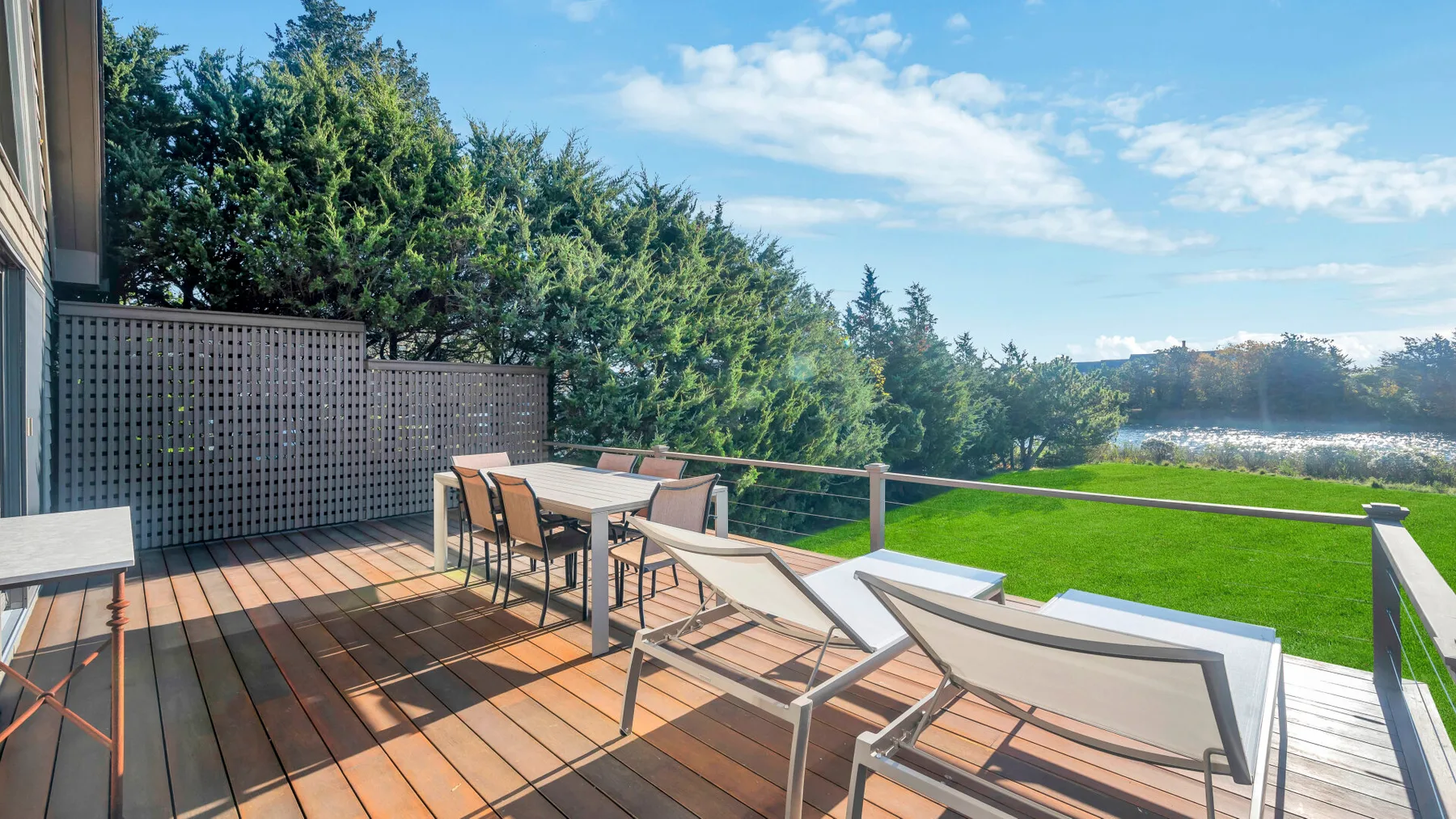 Una terraza de madera tiene asientos al aire libre y una mesa junto a un césped verde.