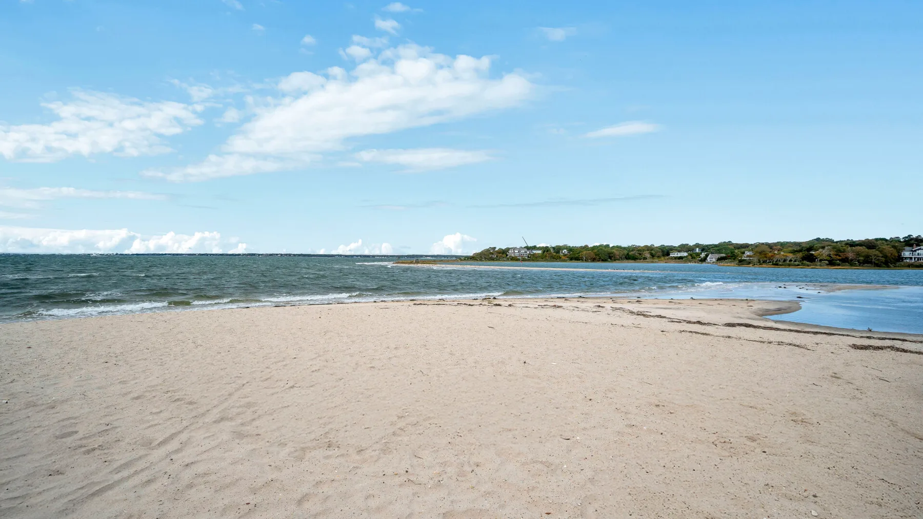 Una playa de arena bordea aguas azules tranquilas bajo un cielo parcialmente nublado.
