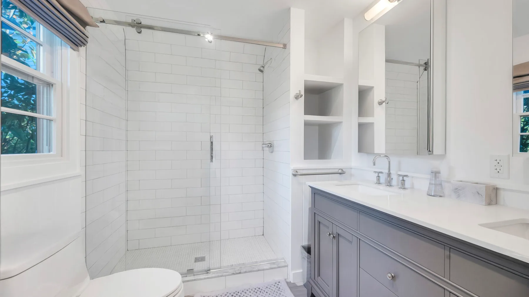 Un baño luminoso con una ducha de vidrio y un lavabo con mueble.