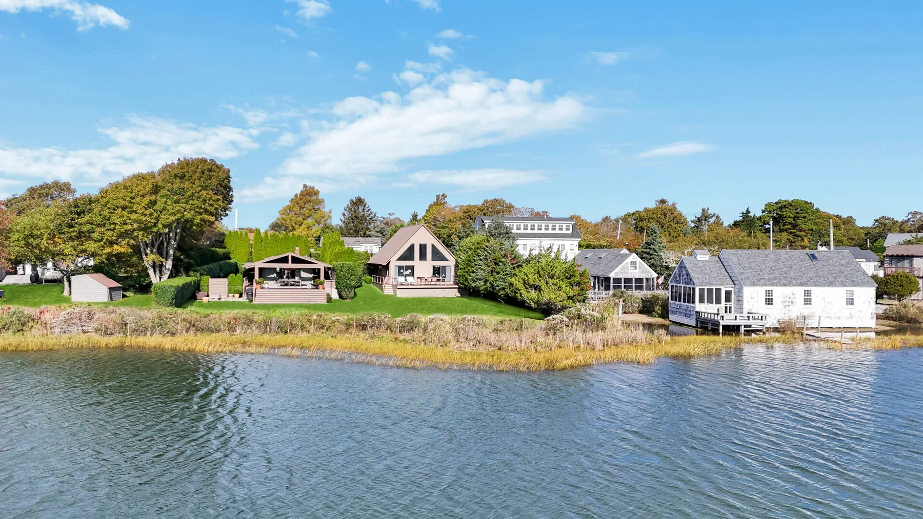 A row of waterfront houses sits along a grassy shoreline beside calm water.