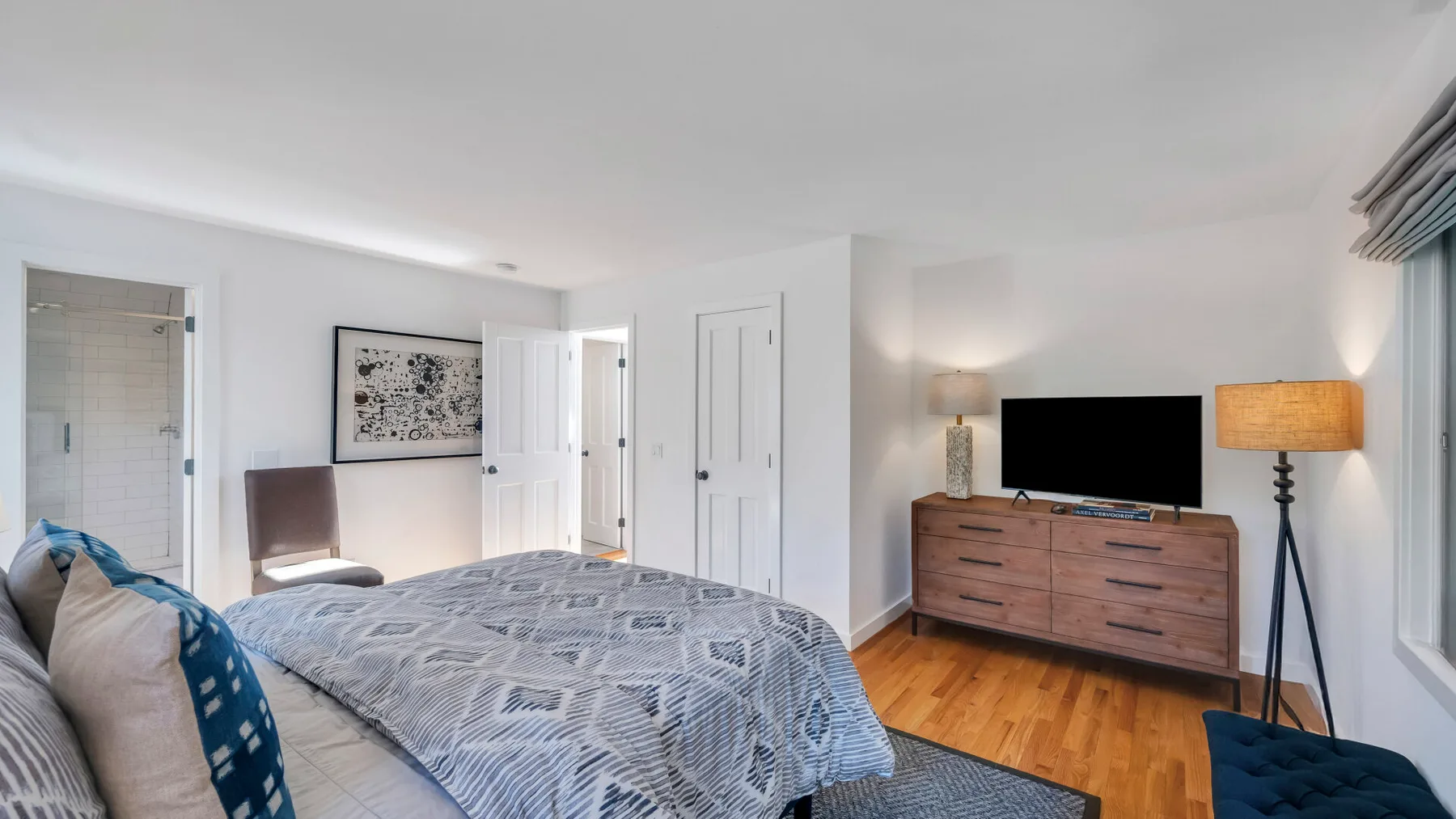 Un dormitorio luminoso con una colcha estampada y un televisor sobre una cómoda.