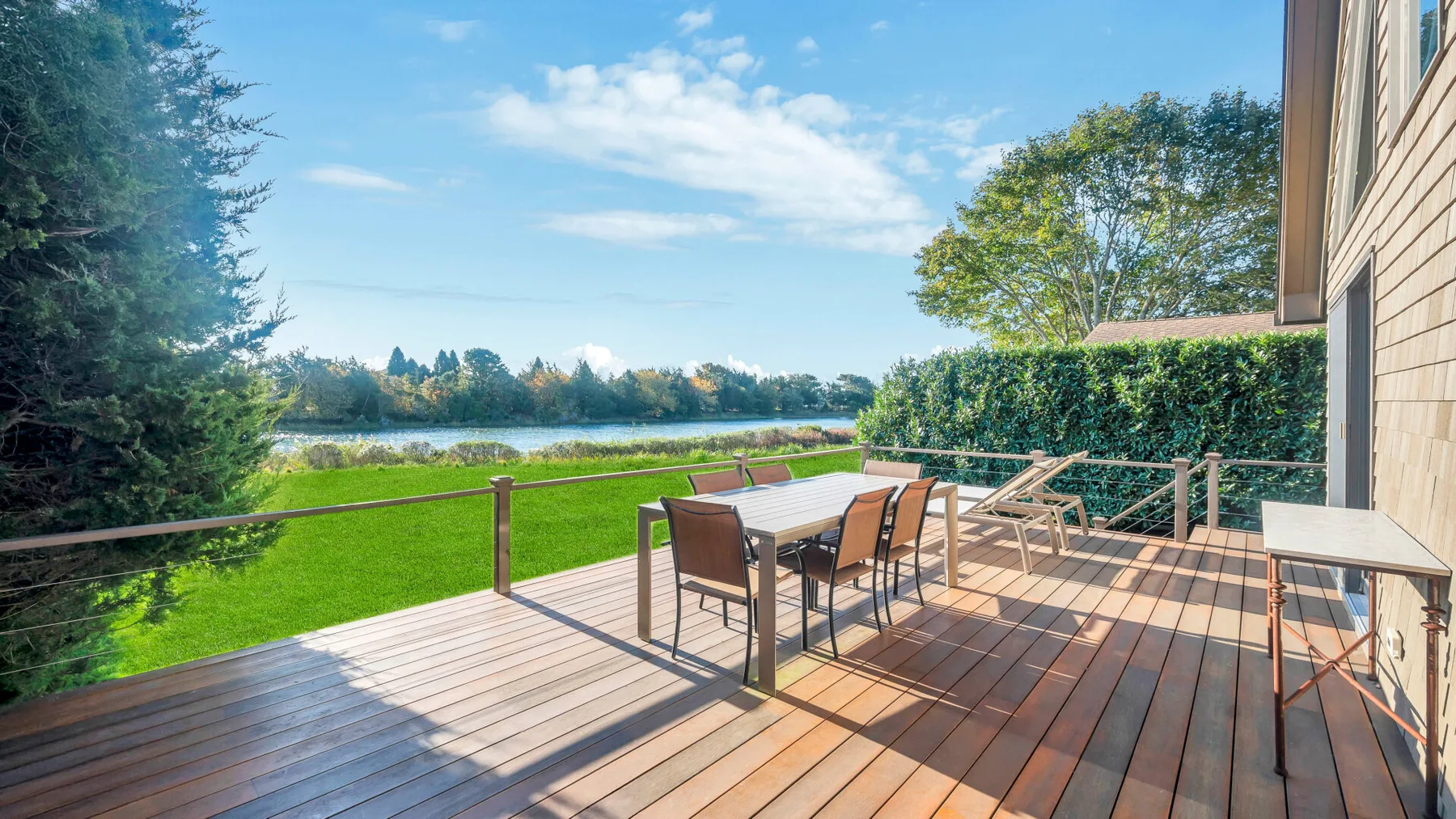 A wooden deck with outdoor seating overlooks a grassy lawn and water.
