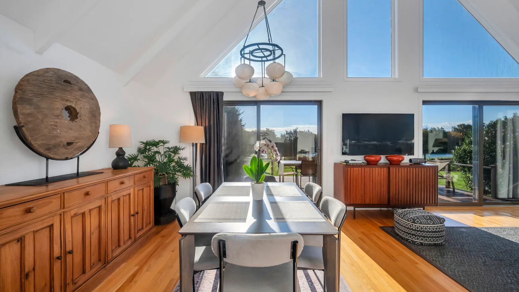 Un comedor luminoso con una mesa larga junto a grandes ventanas y un televisor.