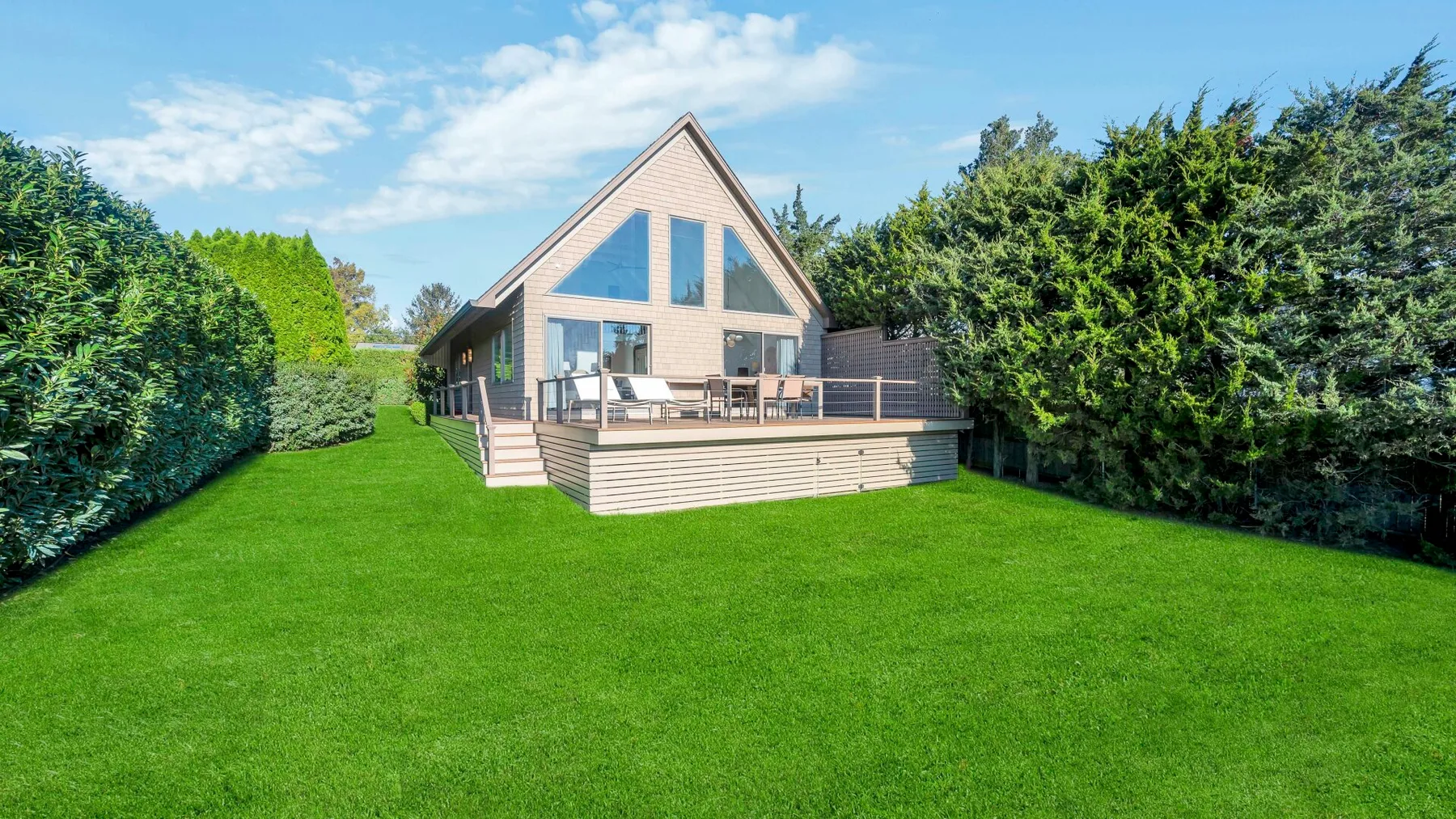 Una casa moderna con una amplia terraza de madera da a un césped verde.