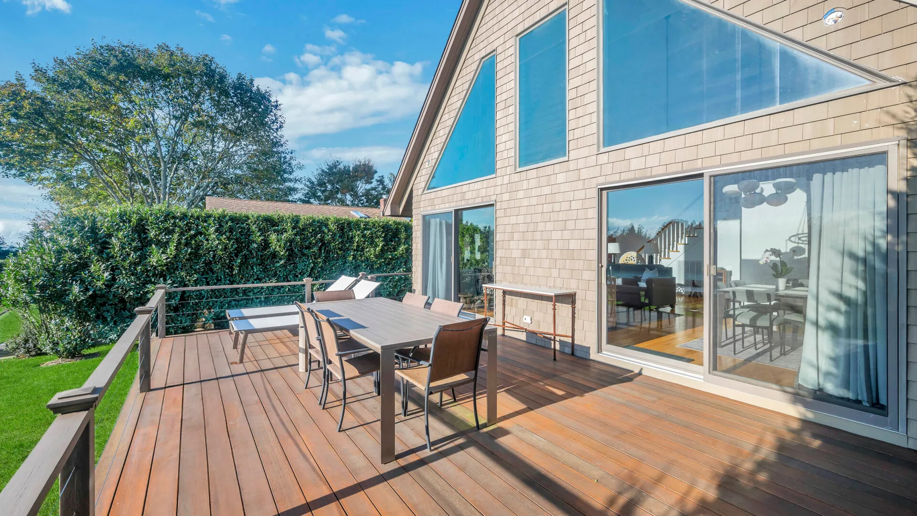 Una terraza de madera con asientos al aire libre junto a una casa y grandes ventanas.