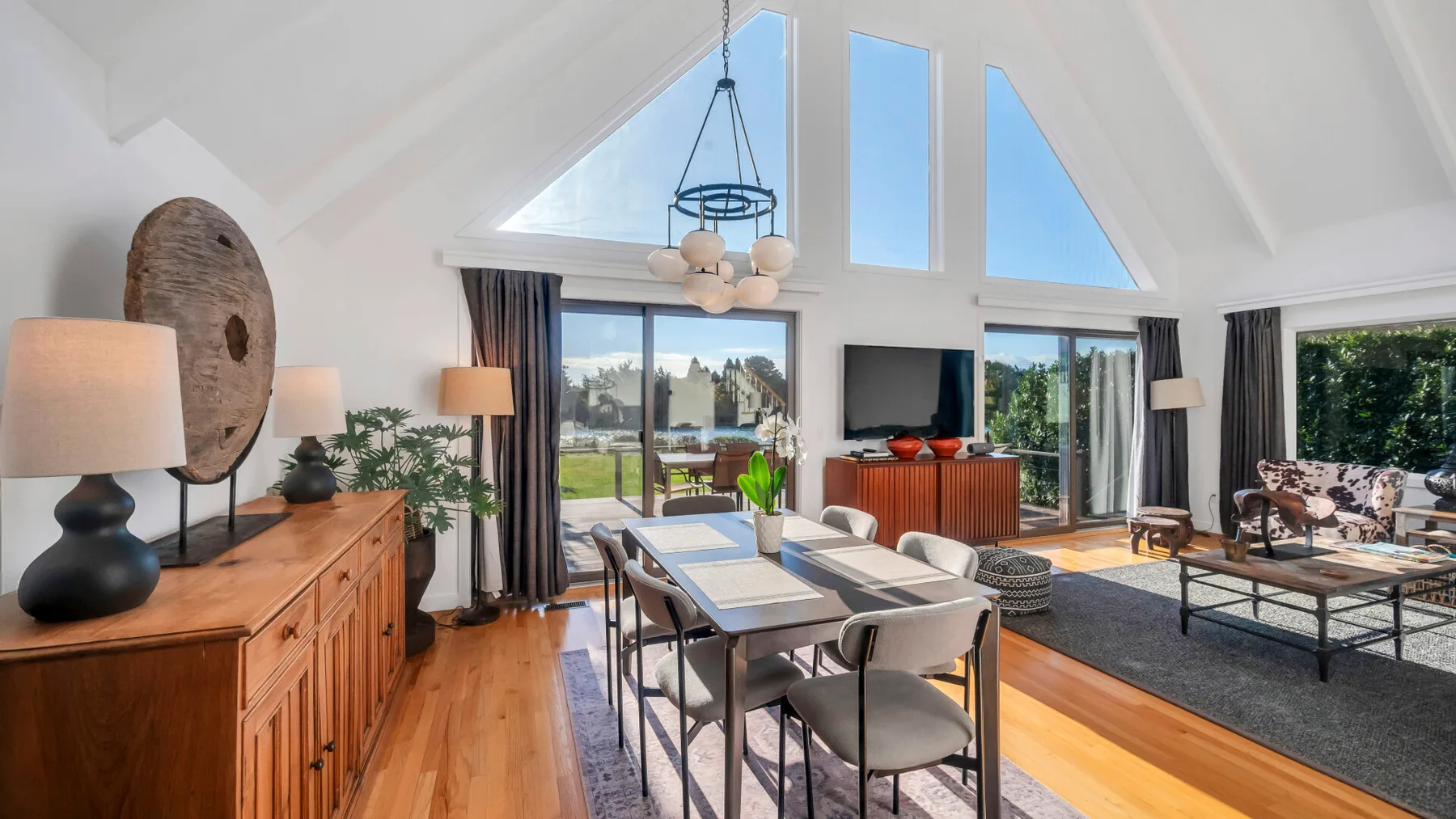 Un luminoso espacio abierto de sala y comedor tiene grandes ventanas y una mesa de comedor.