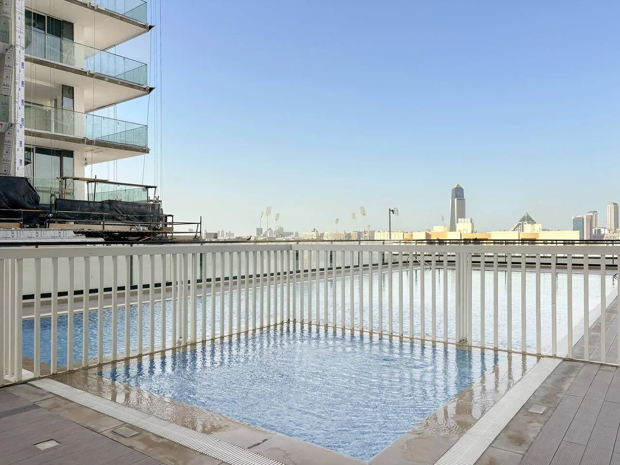 Una piscina en la azotea está junto a una barandilla blanca, con edificios de la ciudad al fondo.