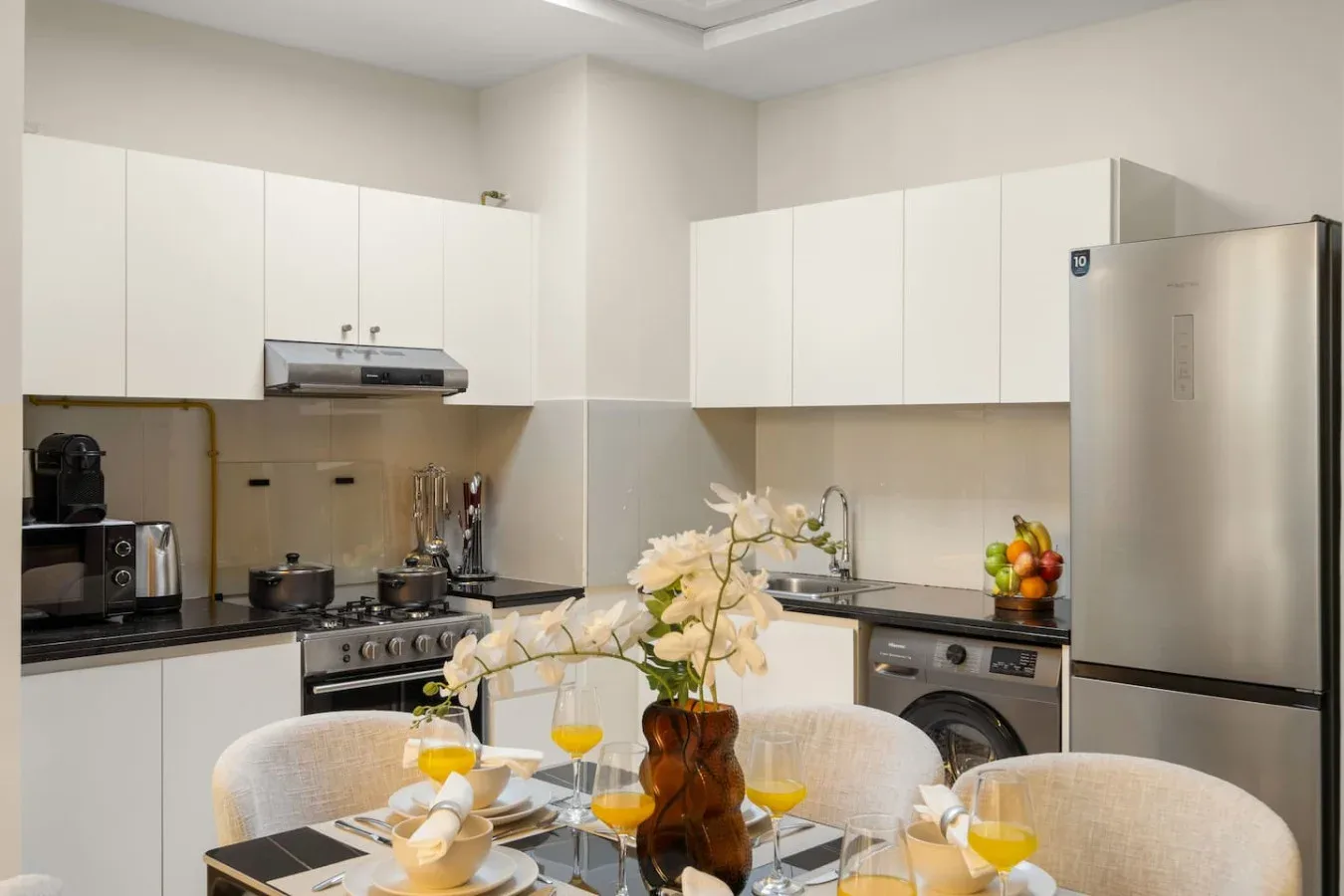 Una cocina luminosa con gabinetes blancos, encimeras oscuras y una mesa de comedor.