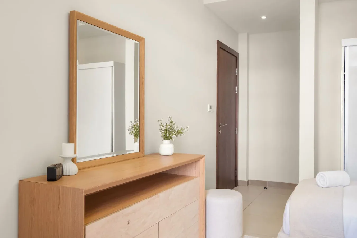 Un dormitorio luminoso con una cómoda de madera, un espejo de pared y parte de una cama.