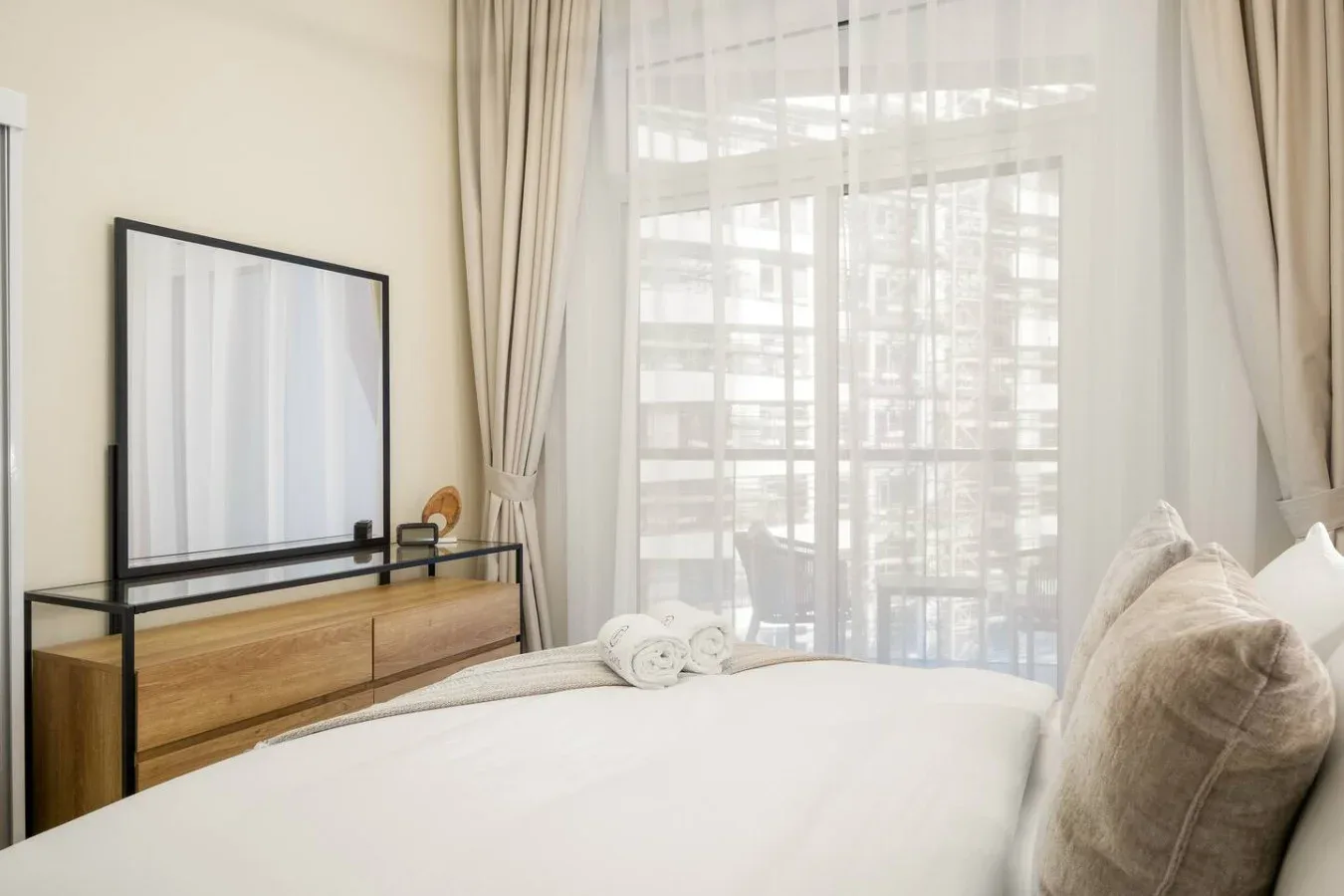 Un dormitorio luminoso con una cama junto a una gran ventana con cortinas.