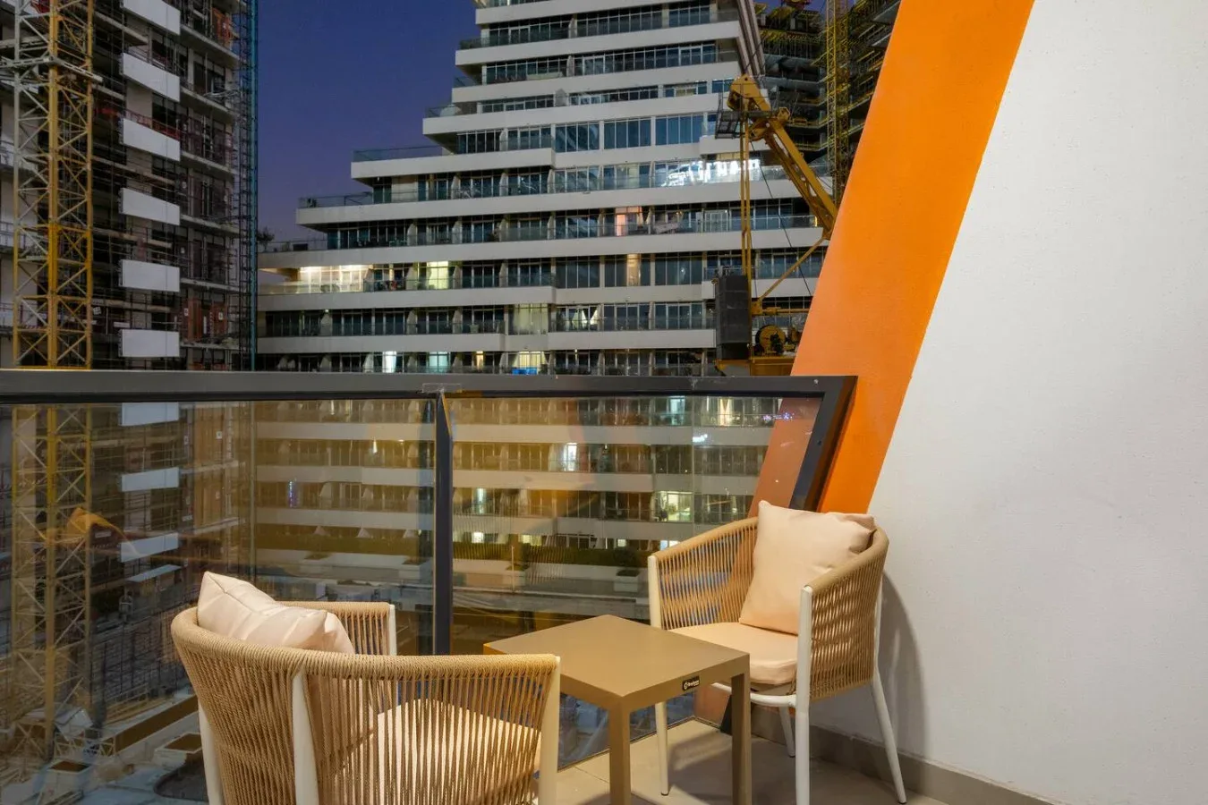 Una zona de asientos en un balcón da a edificios modernos y grúas de construcción.