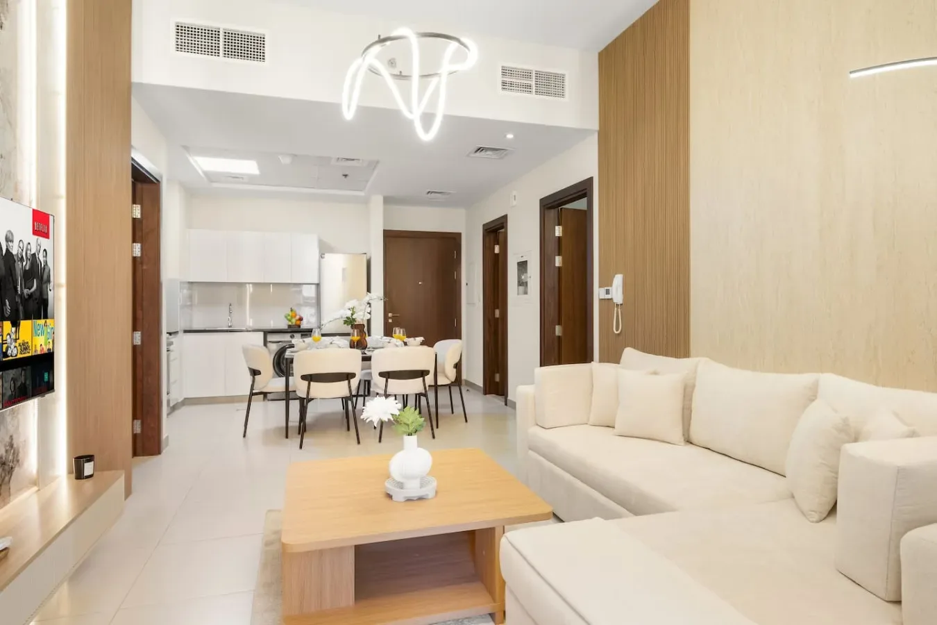 Una luminosa sala de estar se abre a un comedor, con asientos claros y una mesa de centro de madera.