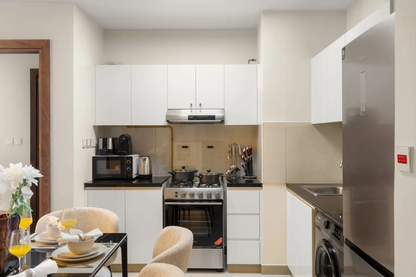 Una cocina compacta con gabinetes blancos, una estufa y una mesa de comedor.
