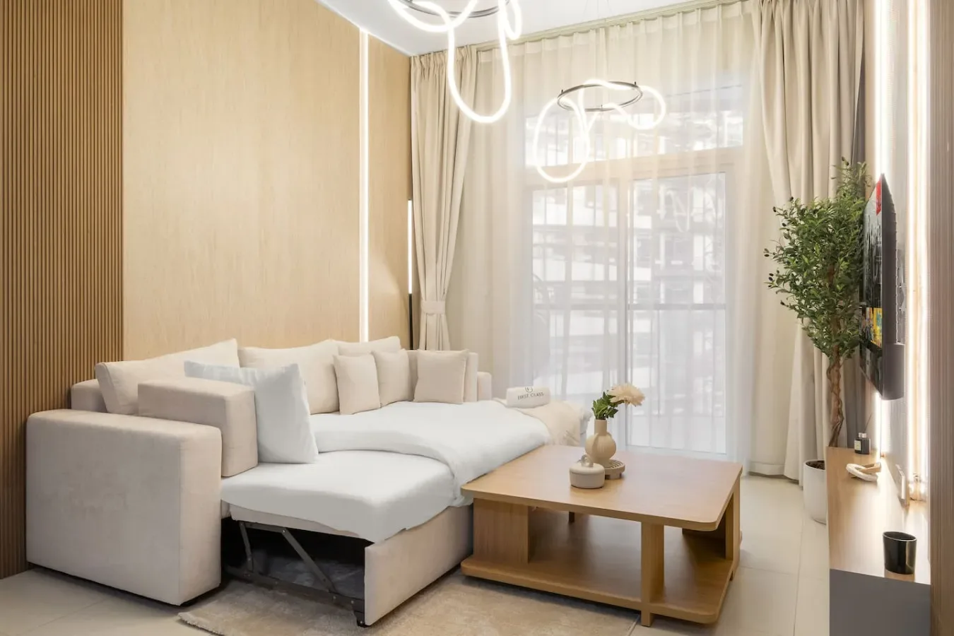 Una sala luminosa con asientos claros, una mesa de centro y grandes ventanas con cortinas.
