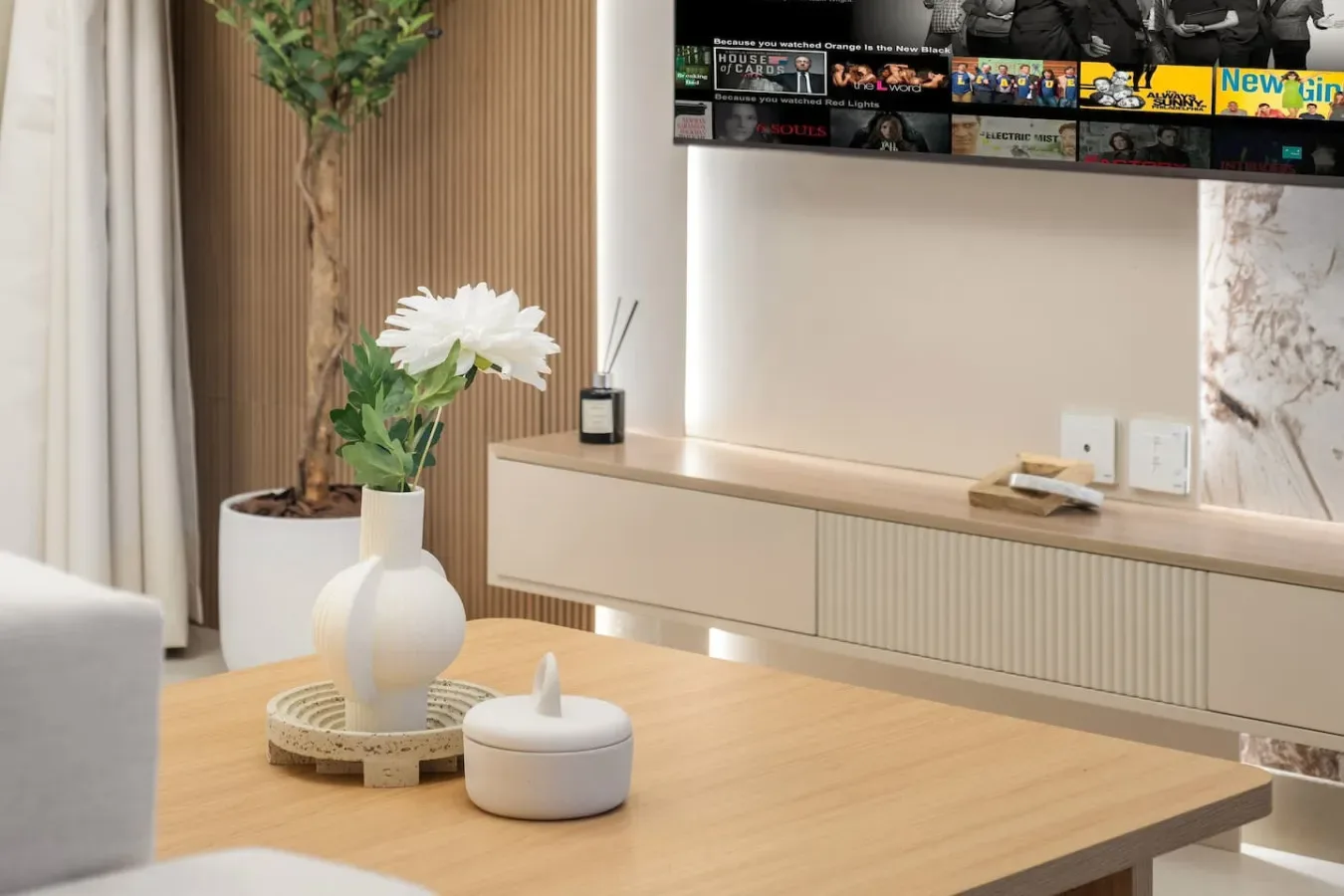 Una sala luminosa con una mesa baja de madera y flores junto al televisor.