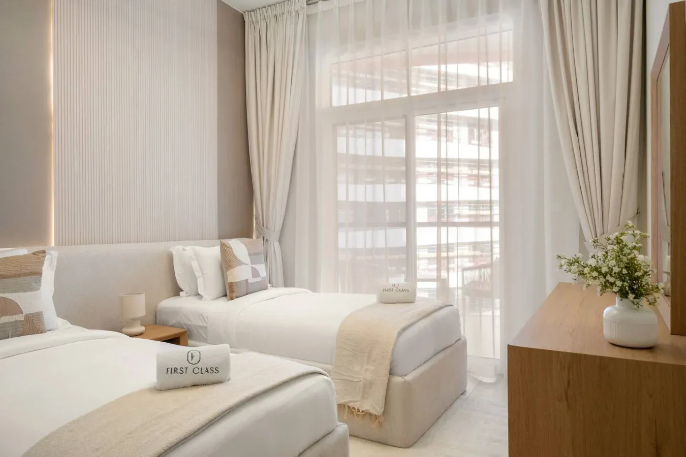 Un dormitorio luminoso con dos camas junto a una gran ventana con cortinas.