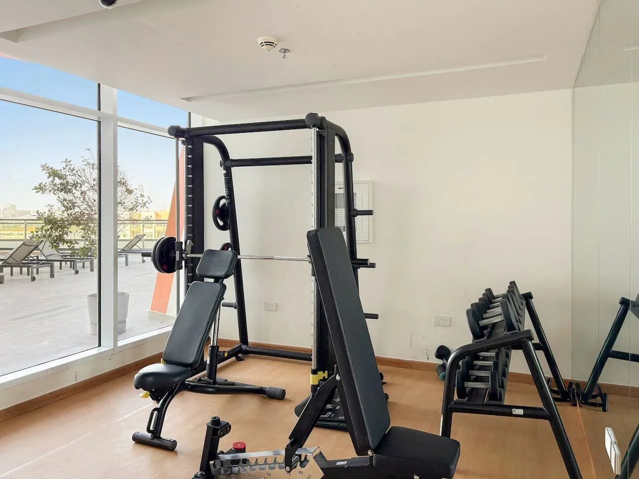 Un gimnasio luminoso con equipos de pesas junto a grandes ventanales.